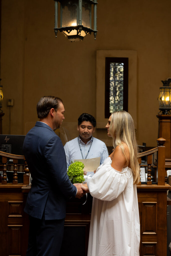 The couple stand facing each other, hands gently clasped, as the officiating pastor stands behind them and they exchange vows.