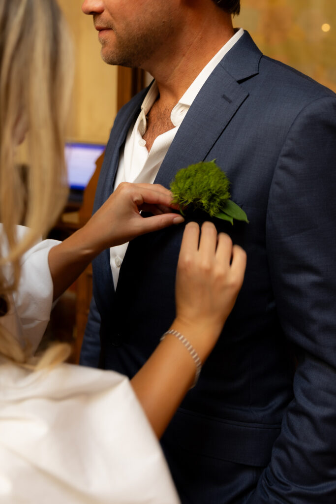Bride pin's her husbands boutonniere on his blue tailored suit.