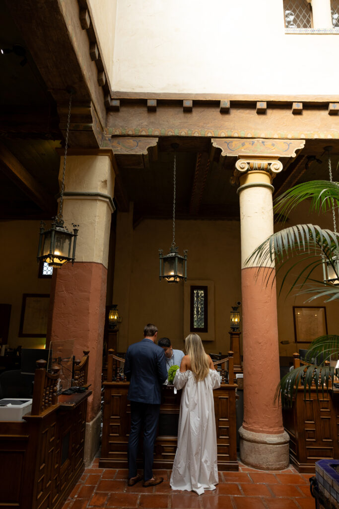 Couple exchanges vows facing each other in a sun-lit courtyard of a private courthouse, framed by terracotta and cream-coloured Ionic-style pillars.