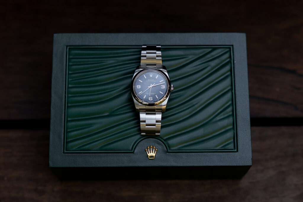 Stainless-steel luxury wristwatch displayed on top of a textured green watch box.