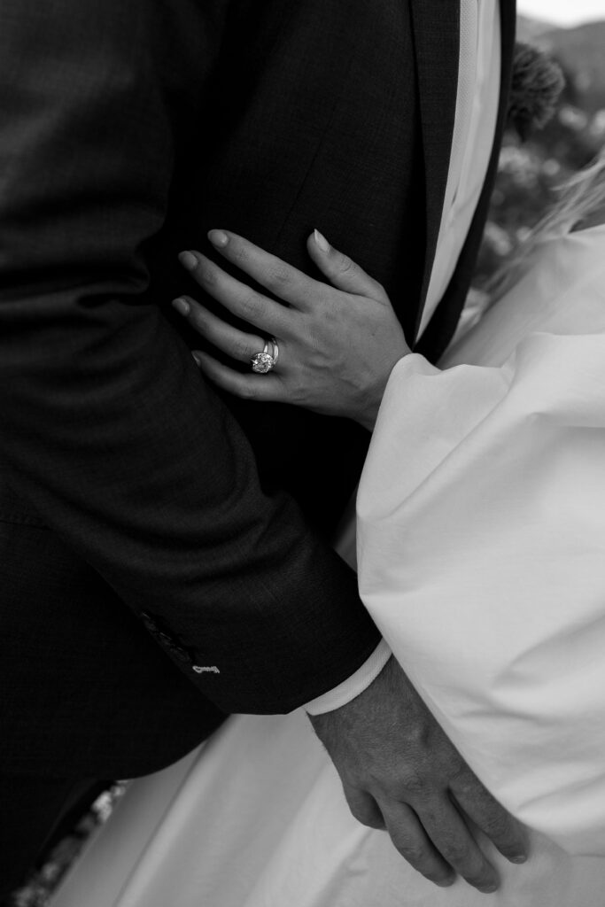 Bride in off-the-shoulder gown and groom walking hand-in-hand on stone pavers at sunset, black and white wedding detail photo.