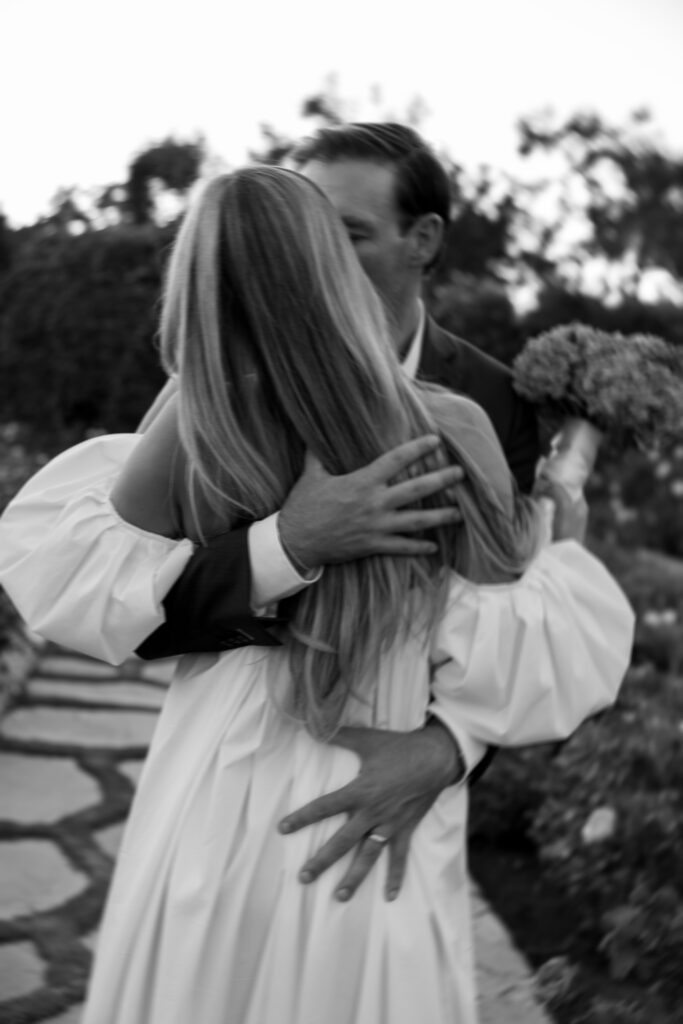 Romantic black-and-white photo of a couple embracing on a garden path during their luxury outdoor wedding in California.