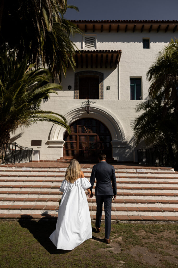 Hand in hand the couple walks towards the private courthouse in a blue suit and off the shoulder bridal gown.