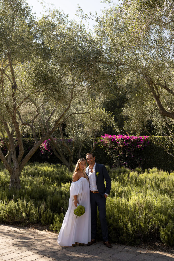 Newlywed's sharing a hug posed in front of a lush green and vibrant garden.