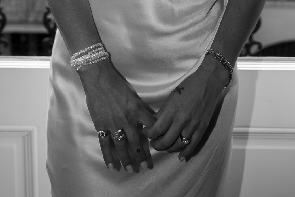 Brides hands are gently holding one another, prior to having the wedding rings on. The photo is solely of her hands and the detailed ripples of her dress behind.