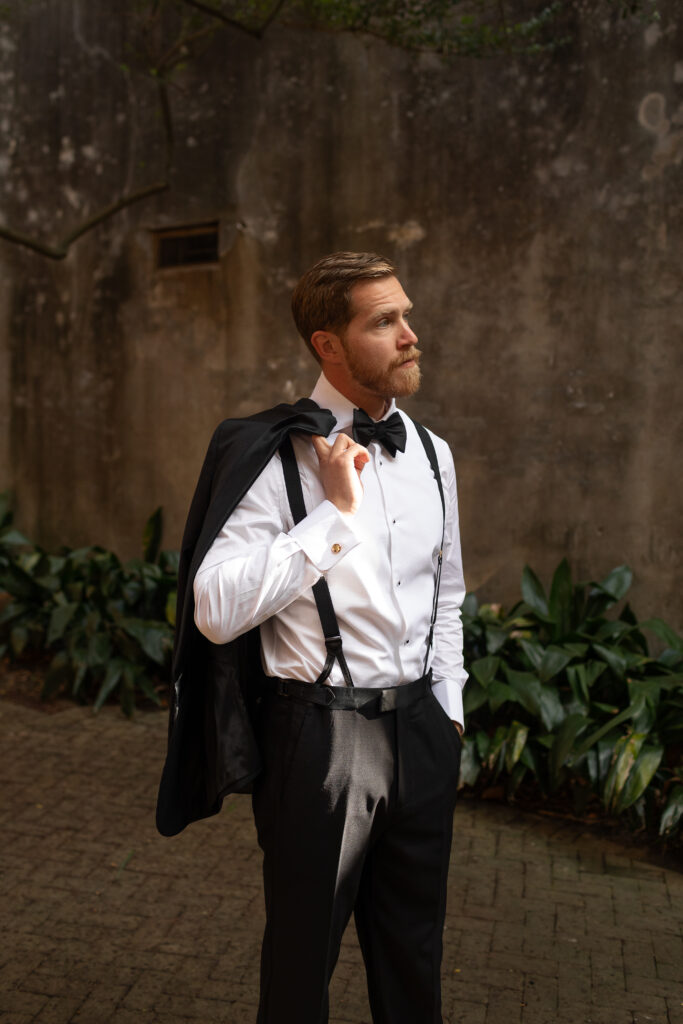 Moody lighting of groom in the concrete corridor, he is looking off into the distance while lightly holding his sport coat over his shoulder prior to the wedding ceremony.