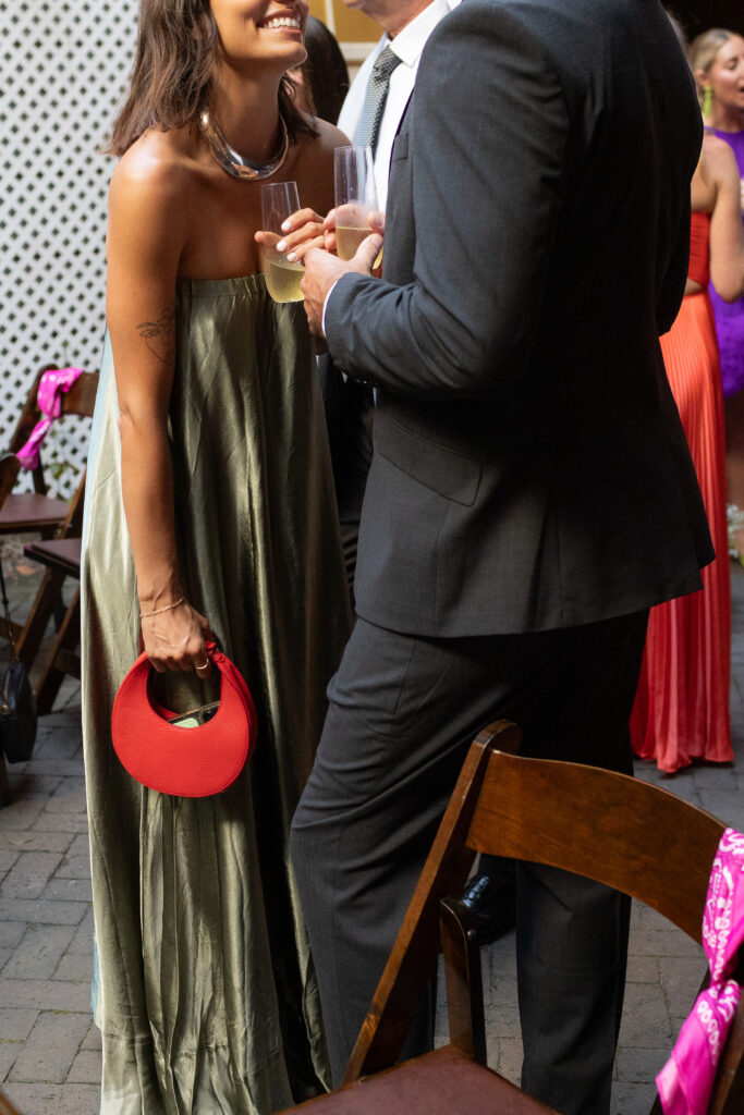 Guests of the wedding sharing a soft smile and laughter during the cocktail hour. Both are drinking from champagne flutes while about to share a kiss. There is an authenticity of shared emotions in this photo, true luxury.