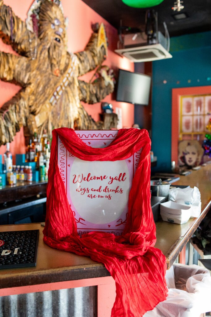 Red scarf draped over a "welcome y'all" sign at the welcome party. Lots of vibrant colors are shown in the photos and decorations on the walls behind.