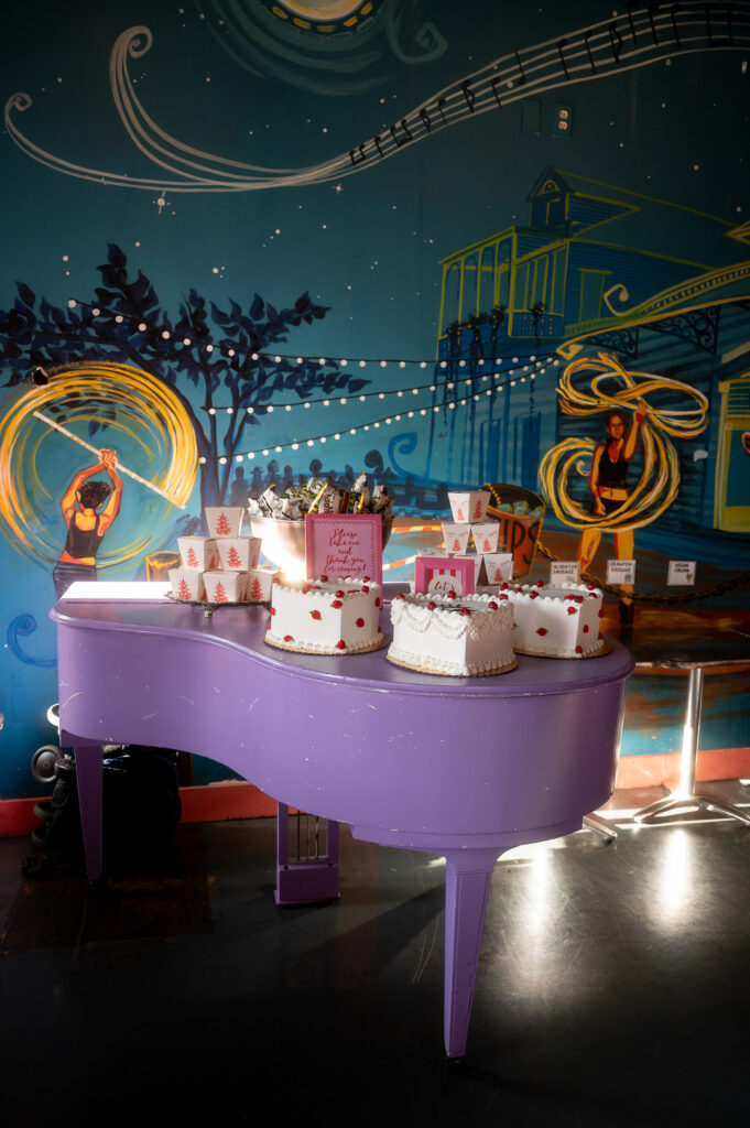 Heart-shaped cakes and Chinese takeout boxes on a purple grand piano, with a vibrant New Orleans nightlife mural backdrop — featured in a New Orleans luxury wedding blog.