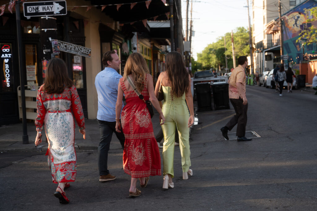 Three guests wearing vibrant blue, red and green outfits walking across a crosswalk toward the welcome reception, featured on a New Orleans luxury wedding blog