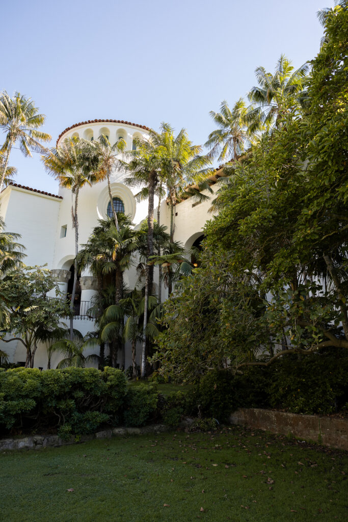 Spanish-style white stucco building surrounded by tall palm trees and lush greenery at San Ysidro Ranch, captured on a sunny day — luxury wedding venue in Santa Barbara.