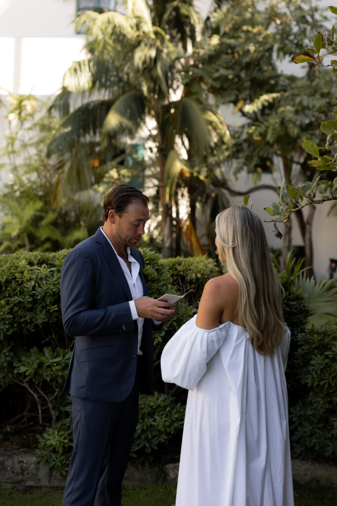 Groom reading handwritten vows to his bride during an intimate wedding moment at San Ysidro Ranch, surrounded by lush tropical greenery and soft natural light — captured by luxury wedding photographer Linden Wilson.