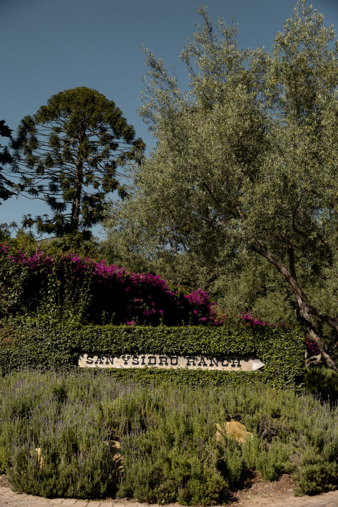 Entrance sign for San Ysidro Ranch surrounded by lush greenery, lavender, and blooming bougainvillea under a clear blue sky — iconic luxury wedding venue in Montecito, California.