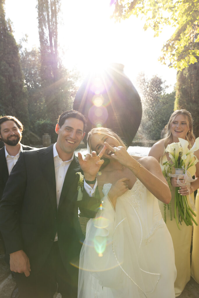 bride and groom showing their wedding rings with a sun burst shining behind them