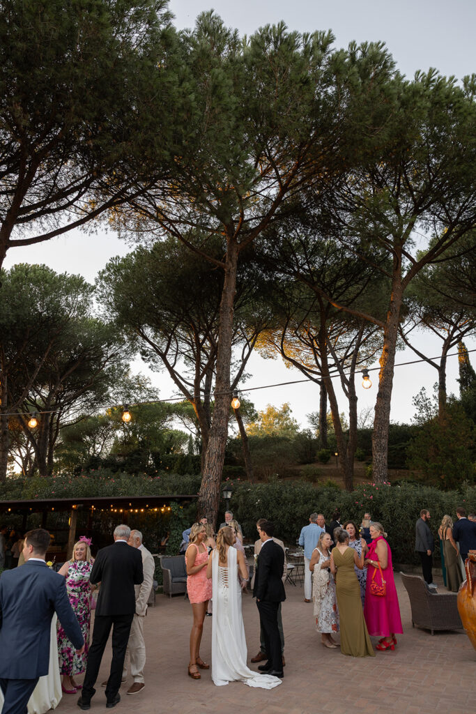 guests at cocktail hour at le 7 fonti with tall trees and lush greenery