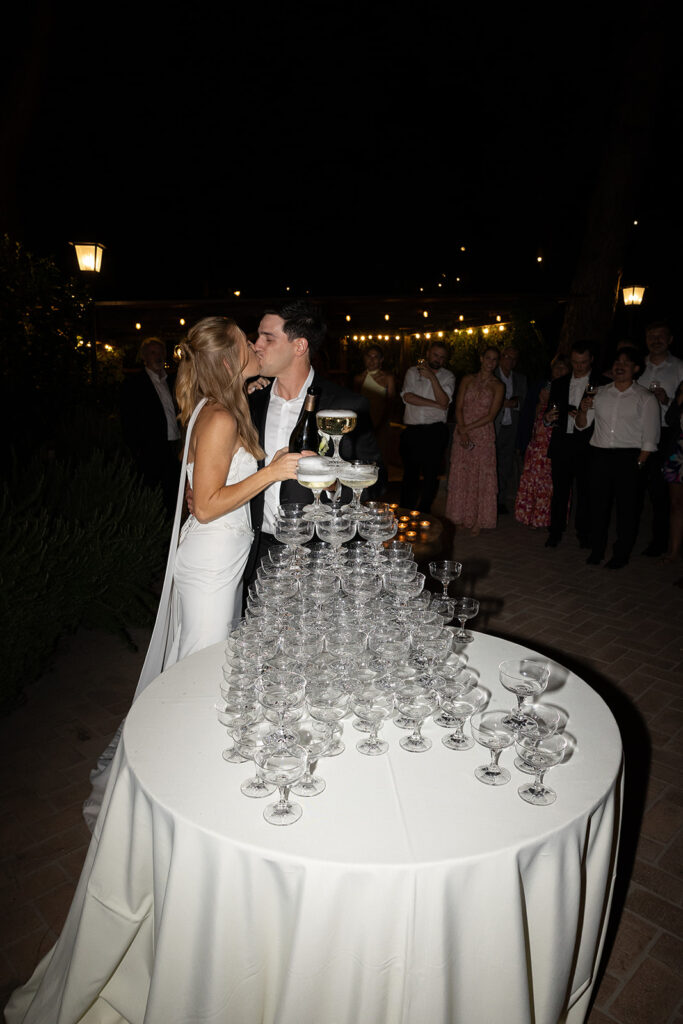 bride and groom share a kiss at the champagne tower at le 7 fonti wedding reception